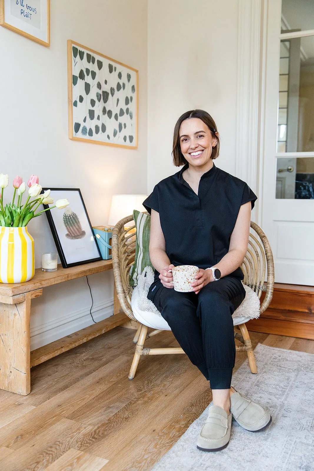 Grace sitting in a rattan chair with a cup of tea, smiling.
